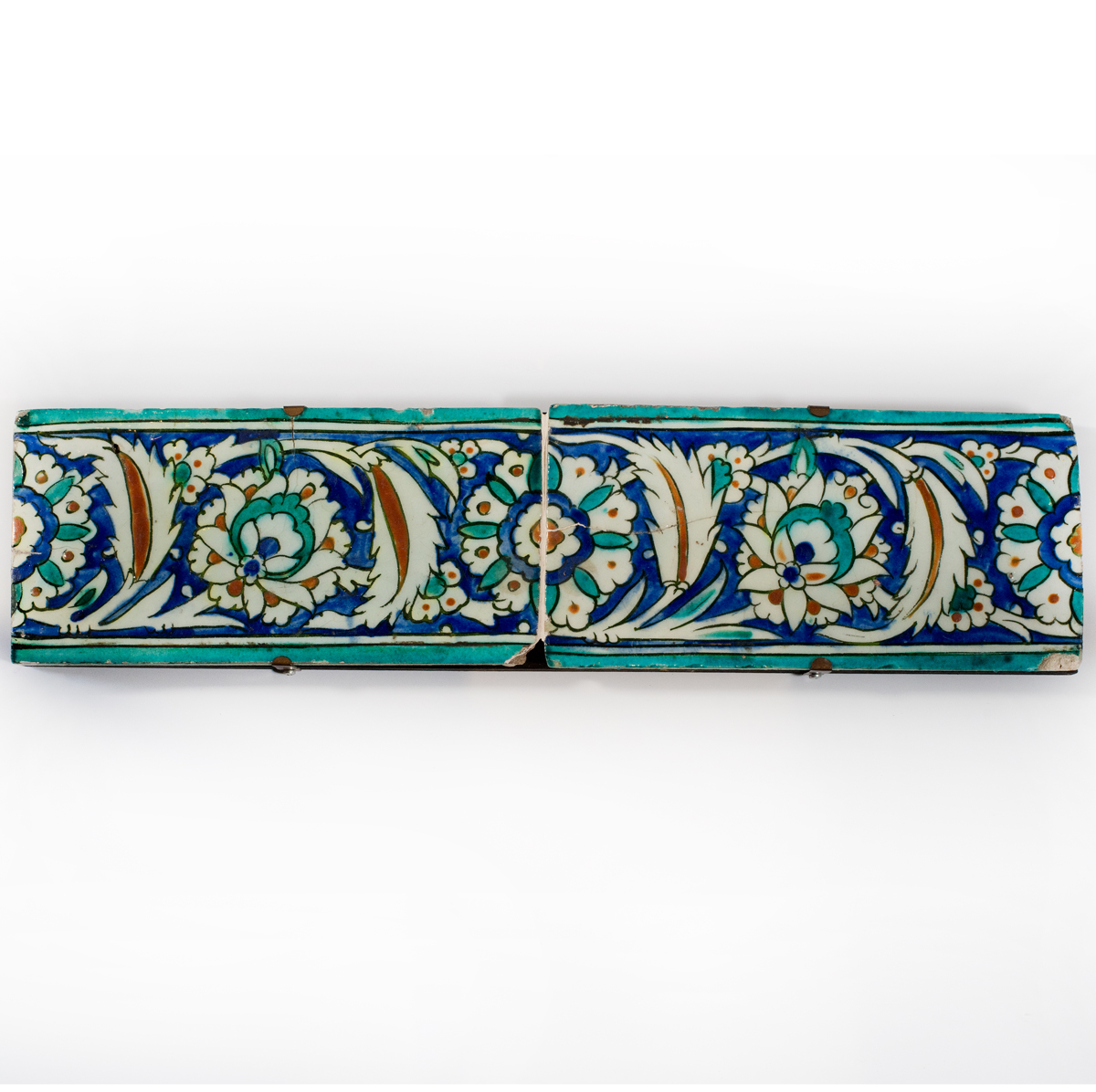 Two Ottoman Iznik border tiles, circa 1600, each of rectangular form, the glazed fritware painted in underglaze turquoise, cobalt blue, black and terracotta red with a continuous band of leafy arabesque scrolls enclosing flowerheads, with turquoise borders mounted Turkish c1600