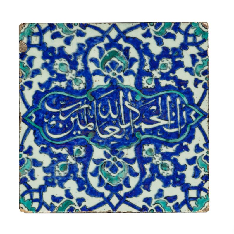 A square Ottoman Empire Iznik tile, the fritware body decorated in underglaze cobalt blue and turquoise on a white ground with a central calligraphic panel inscribed with the 'Alhamdulillah' meaning ‘Praise be to Allah’ on a ground of winged palmettes and split lotus flowerheads. Turkish, 17th century.