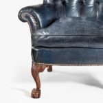 A pair of Chippendale style leather wing armchairs, each with a shaped back, wings and pepper-box arms set above cabriole front legs with acanthus-carved scroll spandrels and out-swept back legs, reupholstered in distressed deep buttoned blue leather details