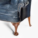 A pair of Chippendale style leather wing armchairs, each with a shaped back, wings and pepper-box arms set above cabriole front legs with acanthus-carved scroll spandrels and out-swept back legs, reupholstered in distressed deep buttoned blue leather
