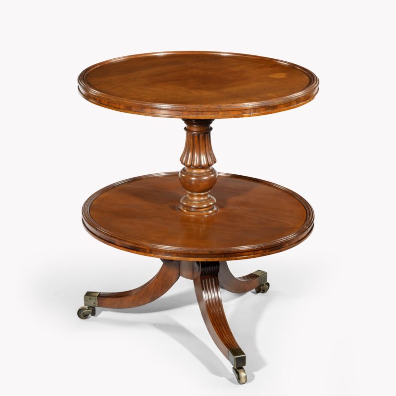 A William IV two tier mahogany table attribruted to Gillows, with two circular shelves, the top one with a dished edge, supported on a reeded and turned baluster column, all on three splayed reeded legs with brass caps and castors