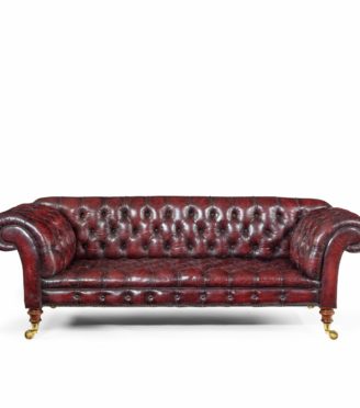 A Victorian deep buttoned Chesterfield settee, with an upright back and scroll arms, set on four turned walnut legs with brass castors, reupholstered in distressed burgundy leather
