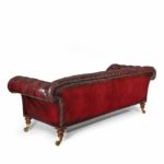 A Victorian deep buttoned Chesterfield settee, with an upright back and scroll arms, set on four turned walnut legs with brass castors, reupholstered in distressed burgundy leather back