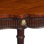 A large Regency mahogany serving table attributed to Gillows, the shaped top above a fluted frieze with four superb ormolu lion’s mask roundels, all raised on six slender, tapering reeded legs - detail