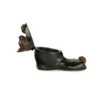 A Black Forest fruitwood carving of a cat in a boot, carved with a cat with inlaid glass eyes resting in the mouth of an ankle boot while the tips of his paws and tail peep out from the open toe of the boot, the boot stained black, the head hinged to form the lid open