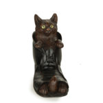 A Black Forest fruitwood carving of a cat in a boot, carved with a cat with inlaid glass eyes resting in the mouth of an ankle boot while the tips of his paws and tail peep out from the open toe of the boot, the boot stained black, the head hinged to form the lid front