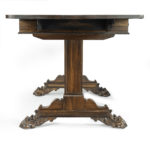 A Regency rosewood end support sofa table, attributed to Gillows, the rectangular top with two hinged flaps veneered in continuous figured veneers, the frieze with two drawers and two dummy drawers, raised on panelled end supports joined by a turned stretcher, with lion’s paw feet. English, circa 1815 side