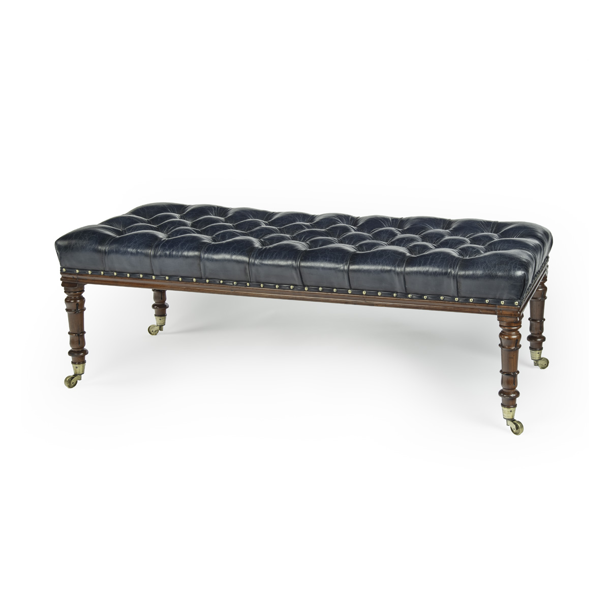 A late Regency mahogany stool, of long rectangular form, the turned tapering legs terminating in the original brass castors, reupholstered in deep buttoned blue leather. English, circa 1815.