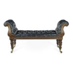A William mahogany bench seat, of long rectangular form, the long seat with an S­ scroll arm at either end, carved with feathery acanthus leaves on the arms and a guilloche border on the frieze, the turned tapering legs terminating in the original brass castors, reupholstered in deep buttoned blue leather.