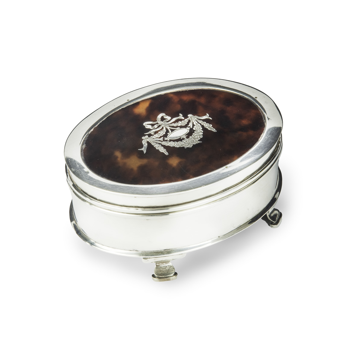 A small oval tortoiseshell piqué patch pot, the hinged lid with a beribboned garland of flowers round a blank escutcheon, raised on four ogee feet. English, assay marks C&A, London, 1919.