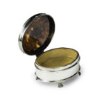 A small oval tortoiseshell piqué patch pot, the hinged lid with a beribboned garland of flowers round a blank escutcheon, raised on four ogee feet. English, assay marks C&A, London, 1919 - Open