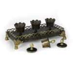 A Louis Philippe bronze and ormolu desk set, comprising two ink wells and a powder shaker in the form of crenelated urns with anthemion-bud finials, all set on a rectangular base with a gallery and applied anthemion scroll and paw feet. French, circa 1840 open