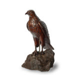 A Black Forest linden wood model of a hawk, standing with wings folded, on a rocky outcrop